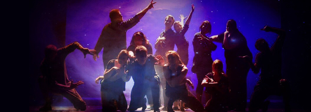 A group of students strike a pose on stage in dramatic lighting.