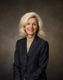 A studio portrait of Dr. Sarah Clemmons, president of Chipola College. She is blonde, posing with her hands crossed in front, wearing a turtleneck and blazer.